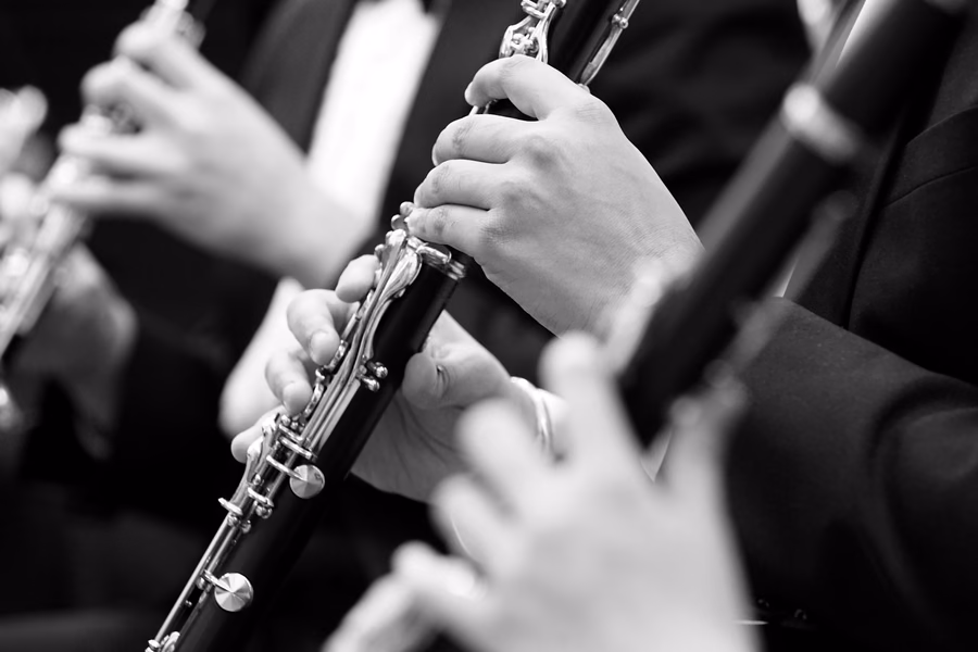 Primer plano en blanco y negro de varios clarinetistas tocando a la vez: se ven las manos sobre las llaves y los cuerpos de los clarinetes.