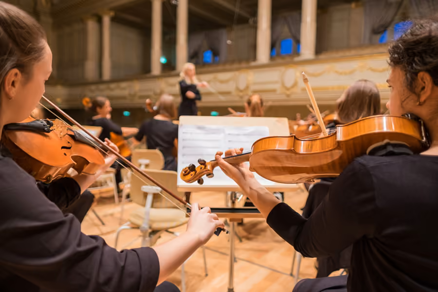 Los músicos de una orquesta durante un ensayo, con el director al fondo.
